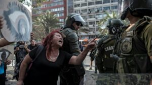 Una mujer se enfrenta a la policía antidisturbios durante una protesta contra el gobierno del presidente chileno, Sebastián Pinera, con carteles que representan unos ojos, en referencia a los manifestantes cuyos ojos han sido alcanzados por perdigones pol