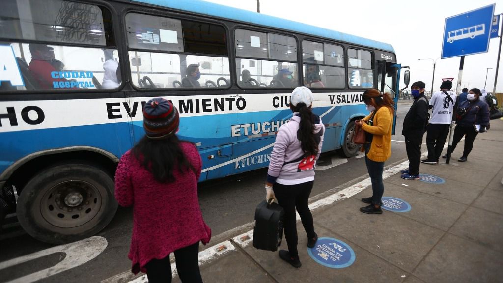 Un grupo de personas mantienen las distancias sociales mientras esperan en una parada de autobús de Lima, Perú