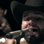Carín León cantando con un micrófono en un escenario