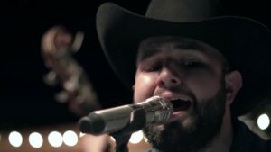 Carín León cantando con un micrófono en un escenario