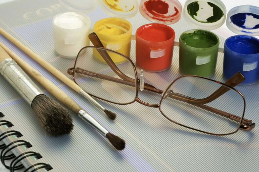 Materiales de arte incluyendo pinceles, pinturas y gafas sobre una superficie