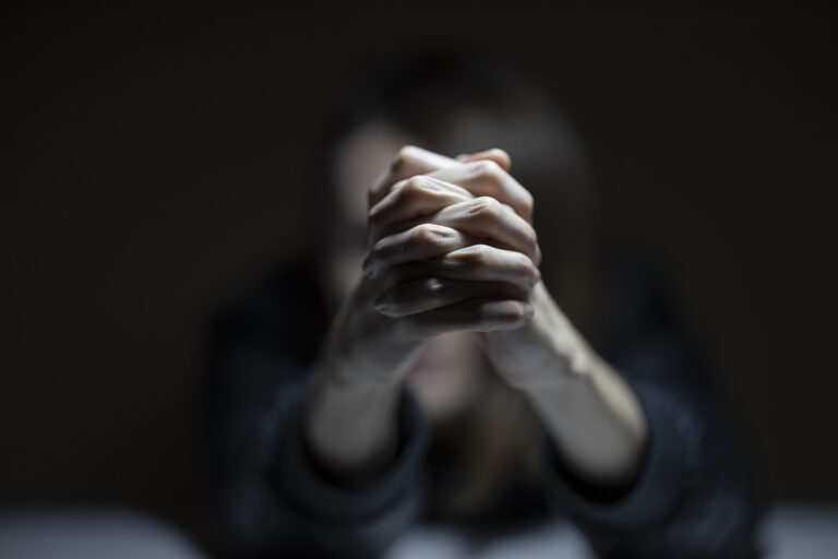 Mujer con las manos entrelazadas en un fondo oscuro
