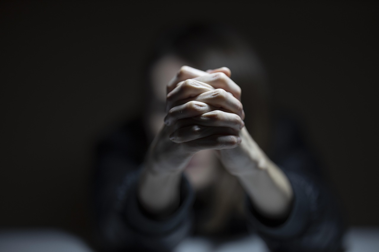 Mujer con las manos entrelazadas en un fondo oscuro